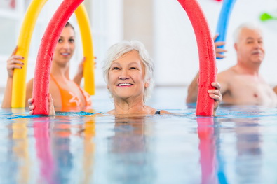 Eine lächelnde Seniorin im Wasser führt eine Übung mit einer Poolnudel aus